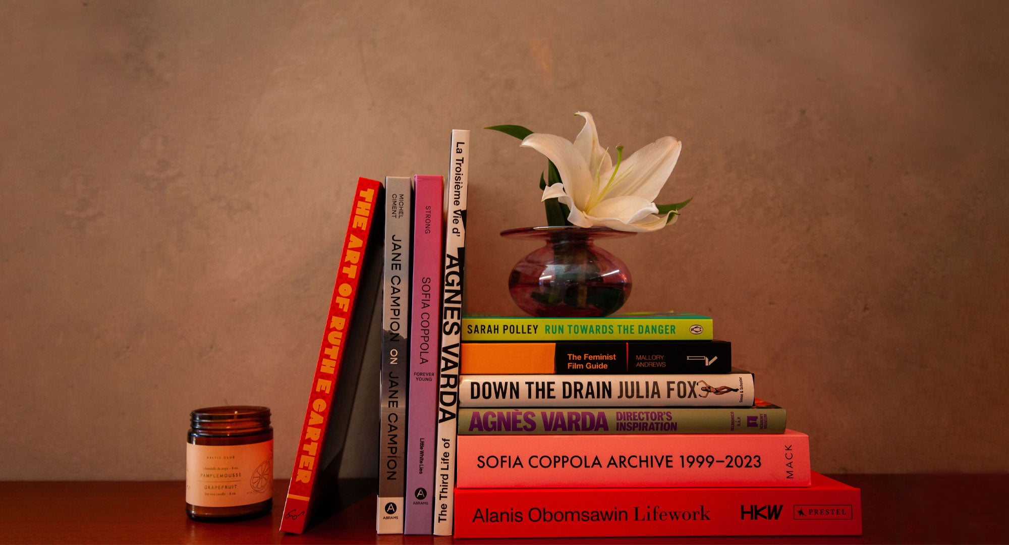 A few stacked books with a potted flower on top and a scented candle to the left