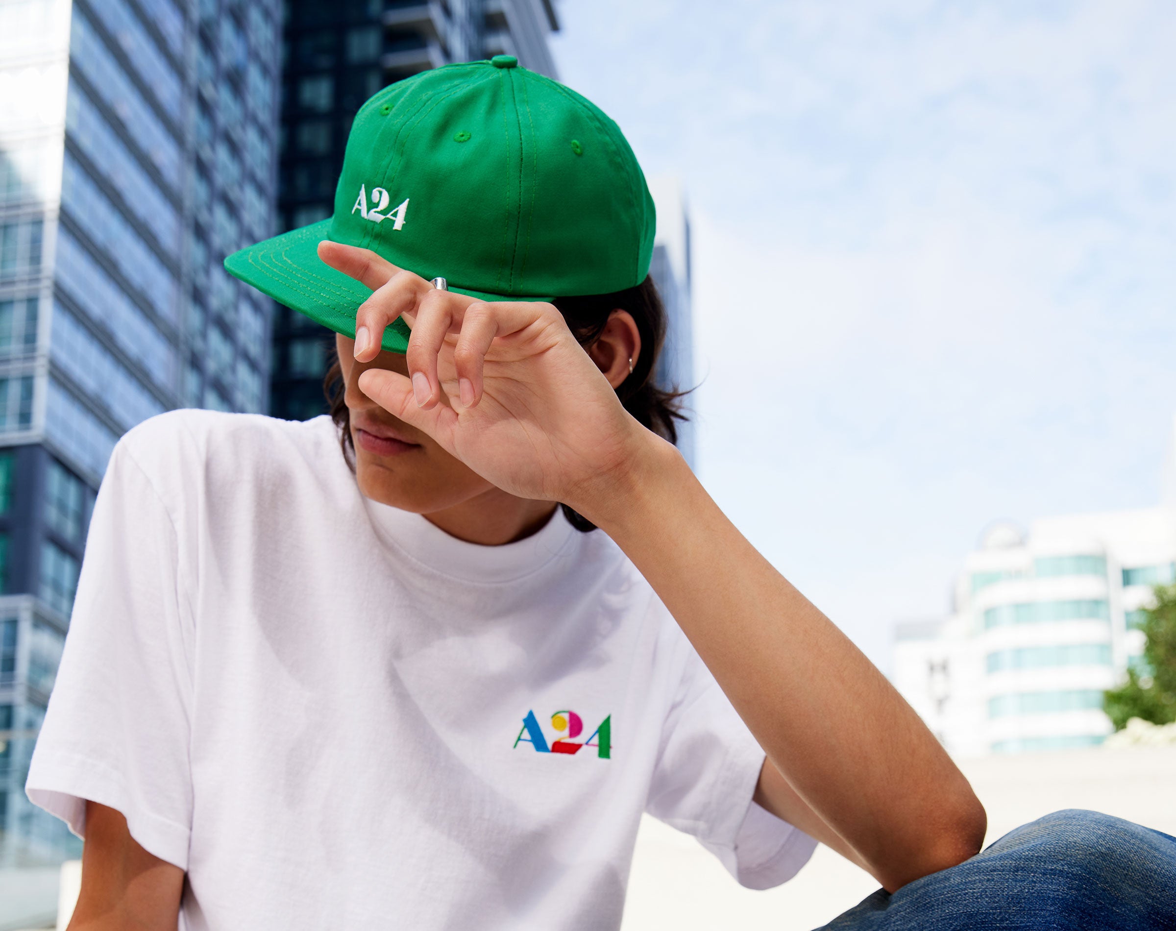 A male model wearing a Kelly Green A24 baseball cap and a white A24 t-shirt