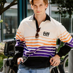 A young man wearing a vintage-style striped rugby shirt with 'tiff' printed on the chest, standing outdoors next to a bicycle.