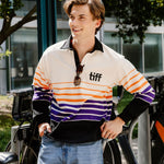 A young man wearing a retro-style striped quarter-zip pullover from TIFF, paired with light-wash blue jeans. He is standing outdoors next to a bicycle, smiling and looking to the side.