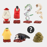 Seven small figurines of various spirits and creatures from the movie Spirited Away are arranged against a plain gray background, with a black circle containing a white question mark representing a hidden "mystery" figure in the se