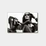 A black-and-white photos featuring Grace Jones posing in a dark hooded outfit, sunglasses, and leather gloves, with one panel showing her reclining with her arms up and the other showing a close-up as she adjusts her sunglasses and holds a flower.