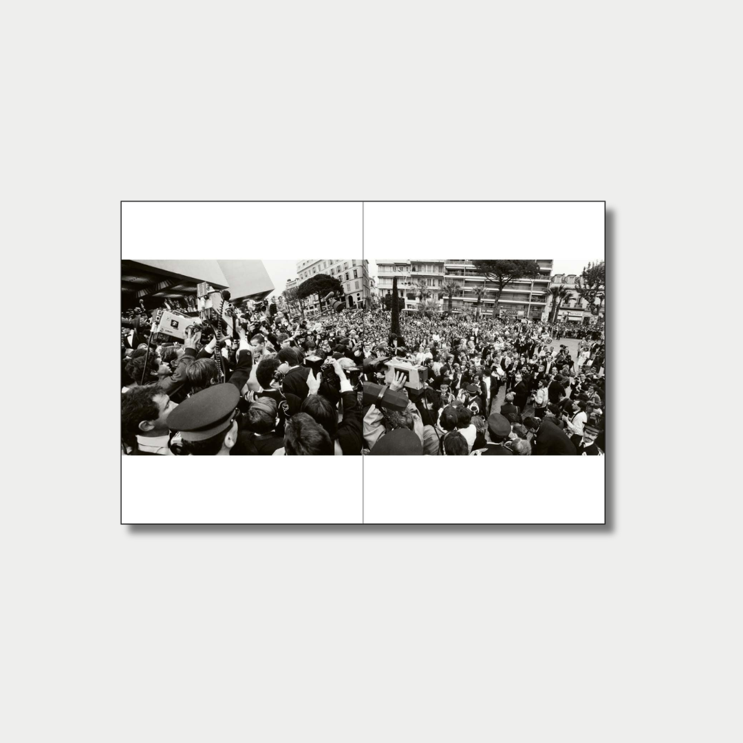 A panoramic black-and-white photograph spread across a two-page book layout captures a dense, chaotic crowd of reporters, photographers holding video cameras, and onlookers gathered outside a building in a city square.