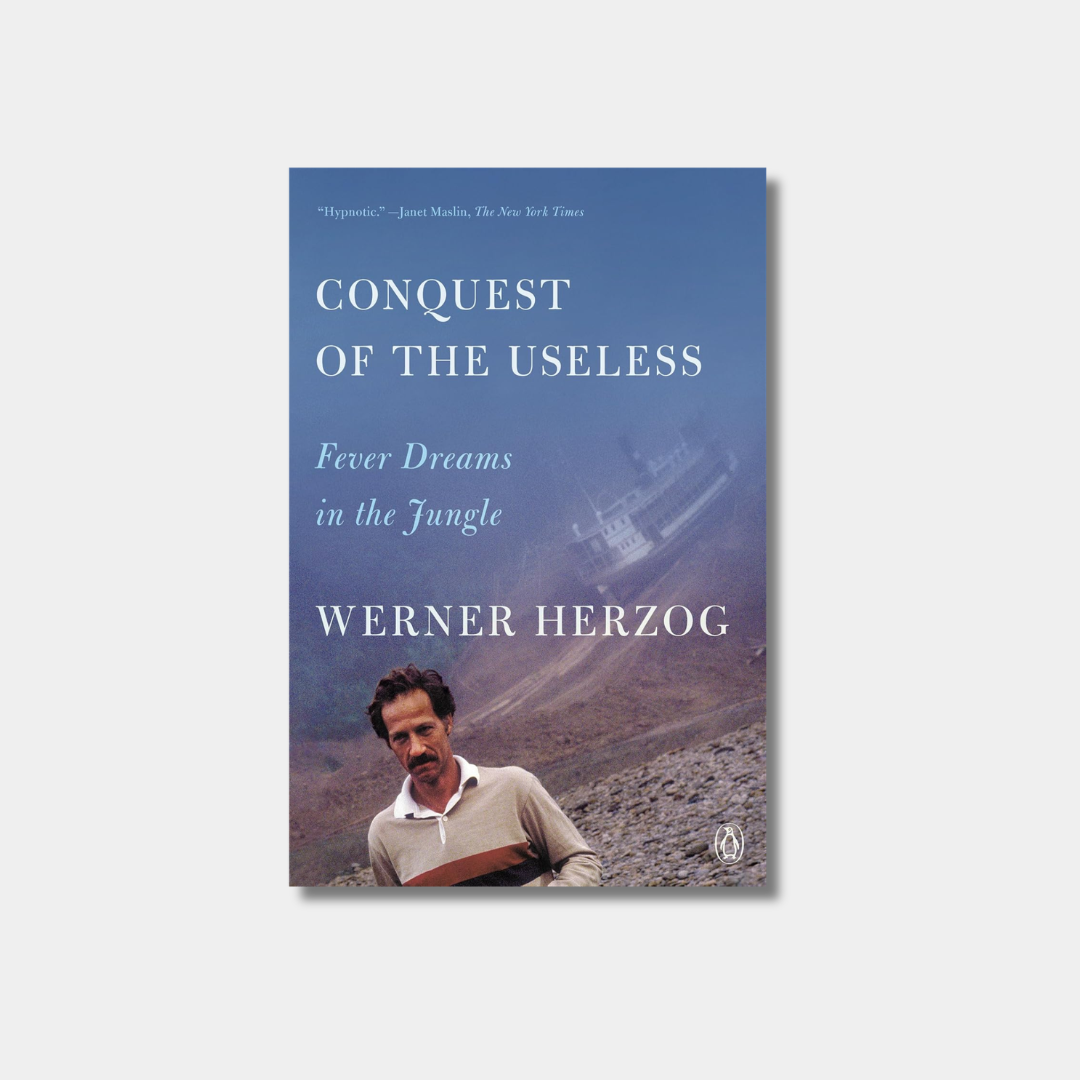 A book cover for "Conquest of the Useless: Fever Dreams in the Jungle" featuring a hazy image of a large ship being hauled over a muddy hill and a portrait of Herzog at the bottom.
