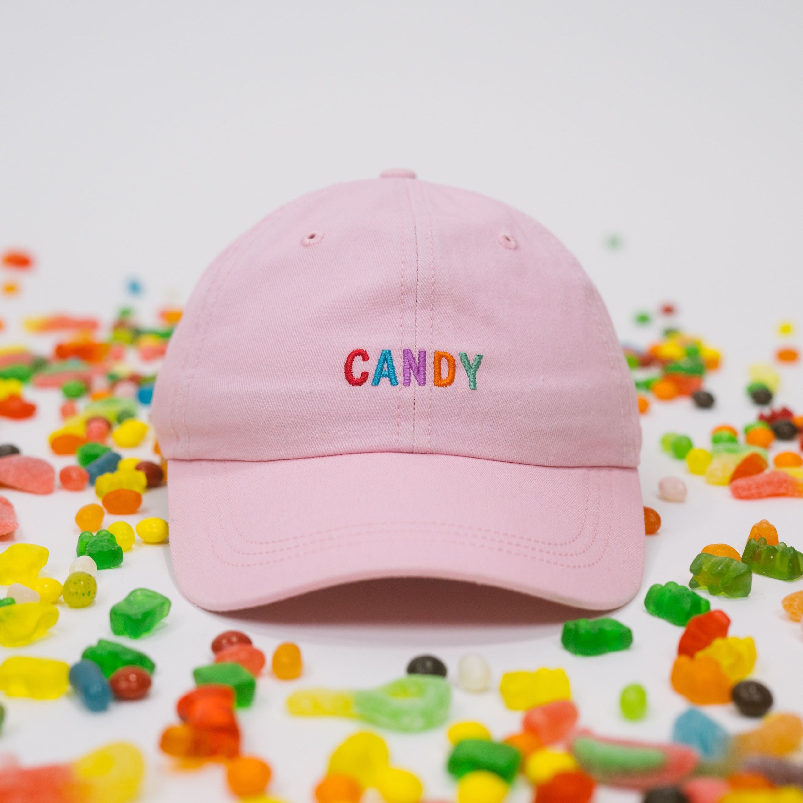 Pink baseball cap on a white background with assorted candies, featuring “Candy” embroidered in multicolour on the front.