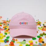 Pink baseball cap on a white background with assorted candies, featuring “Candy” embroidered in multicolour on the front.