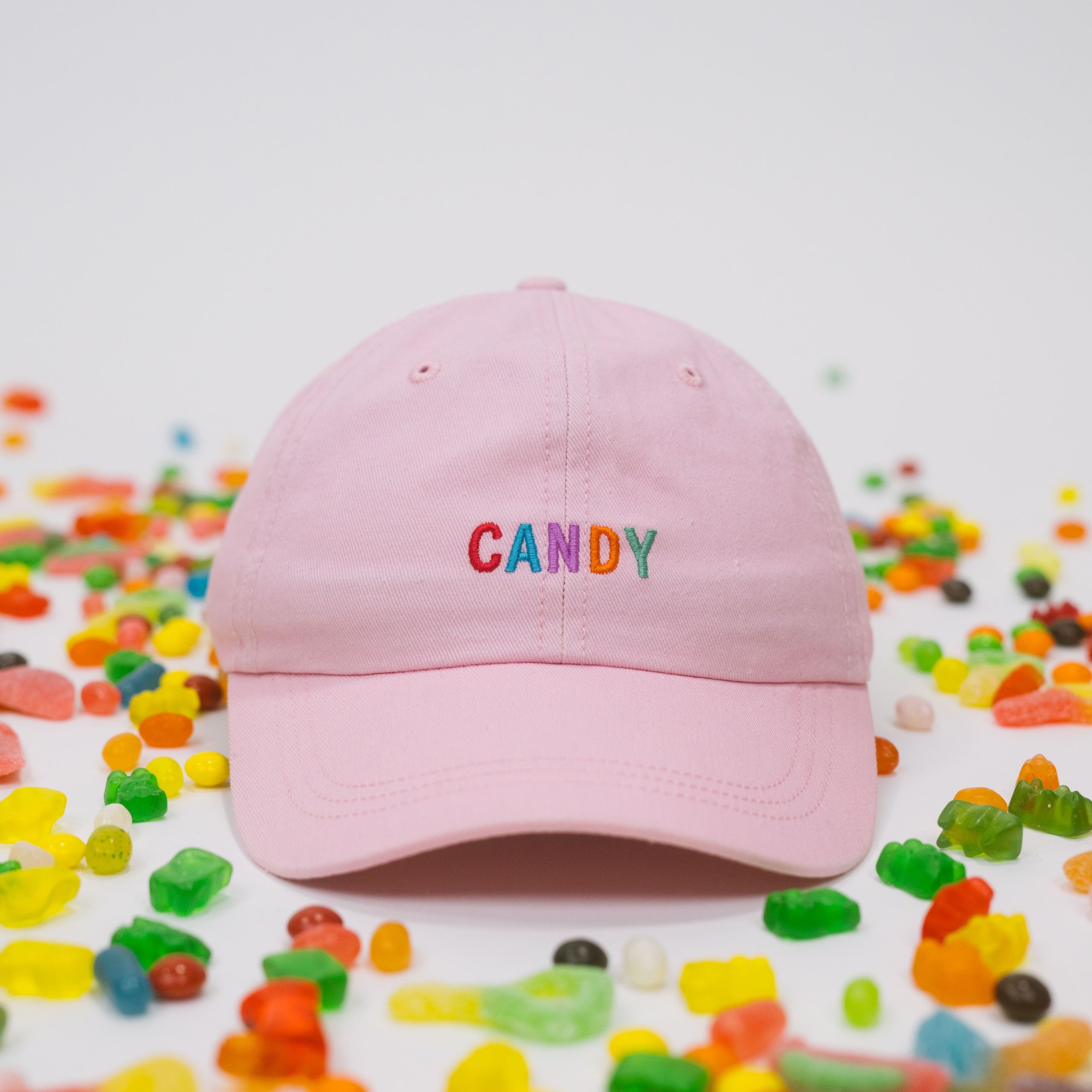 Pink baseball cap on a white background with assorted candies, featuring “Candy” embroidered in multicolour on the front.