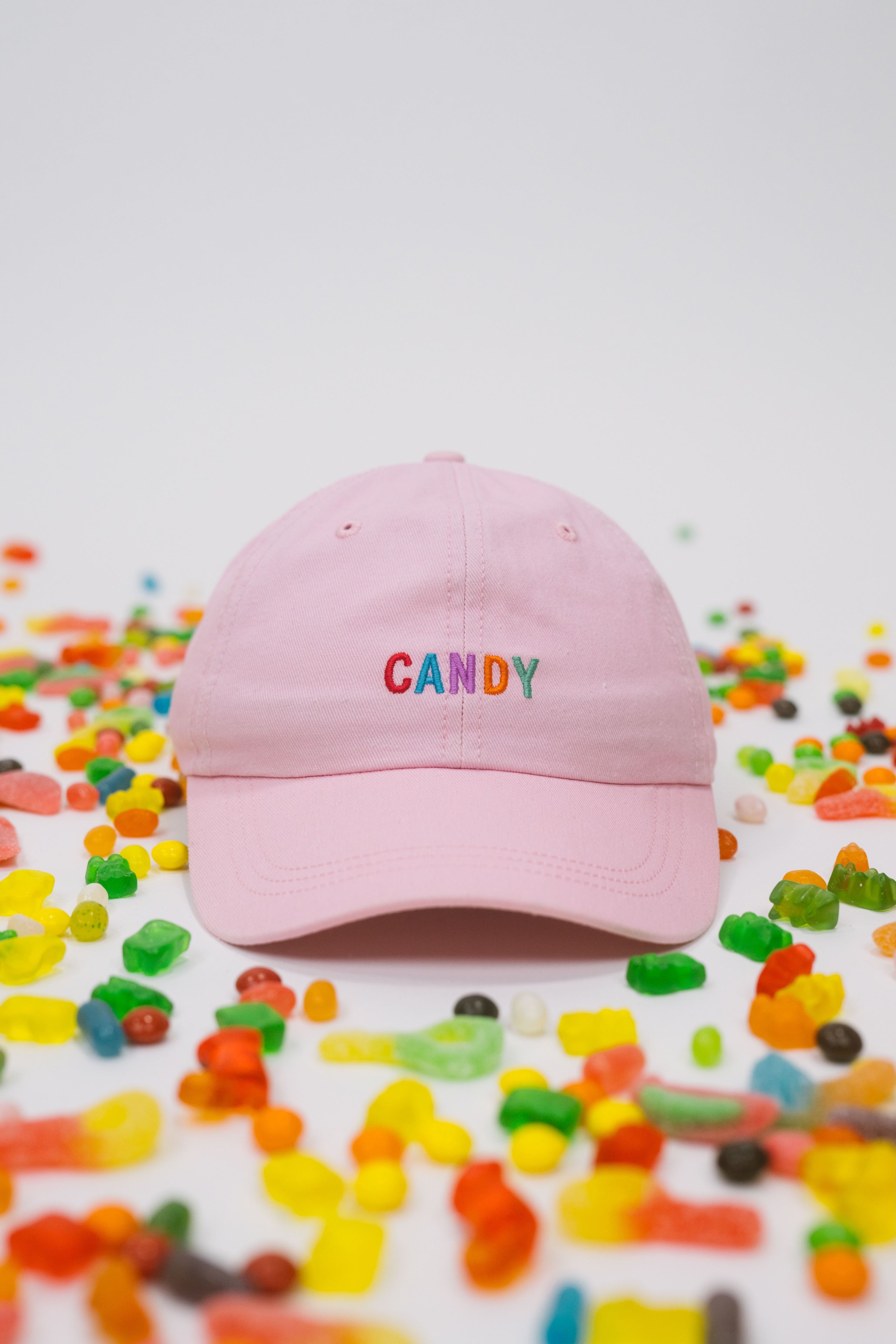 Pink baseball cap on a white background with assorted candies, featuring “Candy” embroidered in multicolour on the front.