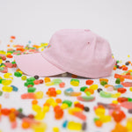 Side profile of pink baseball cap on a white background with assorted candies, featuring “Candy” embroidered in multicolour on the front.