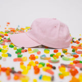 Side profile of pink baseball cap on a white background with assorted candies, featuring “Candy” embroidered in multicolour on the front.