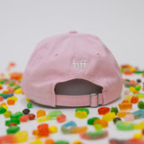 Back view of pink baseball cap on a white background with assorted candies, featuring “TIFF” embroidered in white.