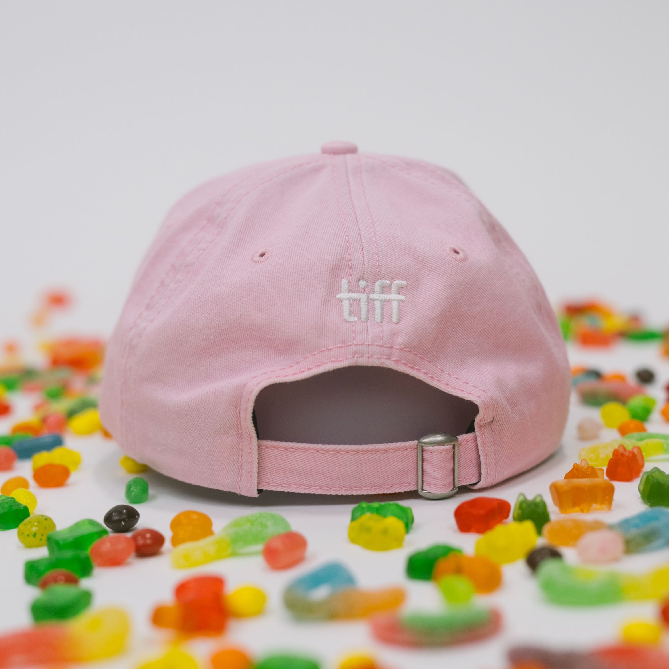 Back view of pink baseball cap on a white background with assorted candies, featuring “TIFF” embroidered in white.