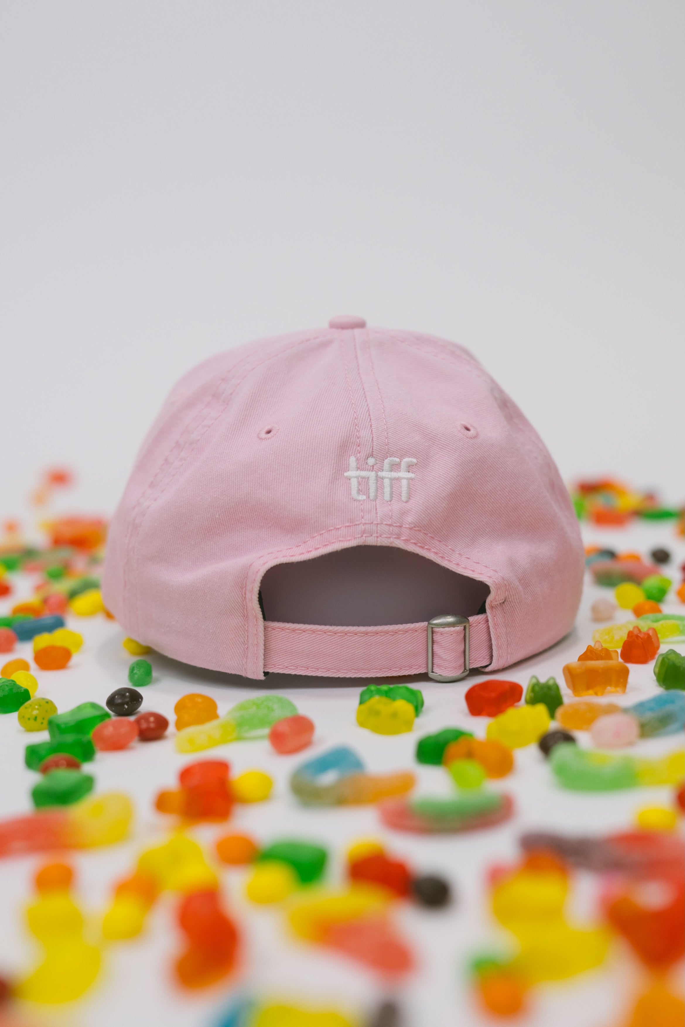 Back view of pink baseball cap on a white background with assorted candies, featuring “TIFF” embroidered in white.