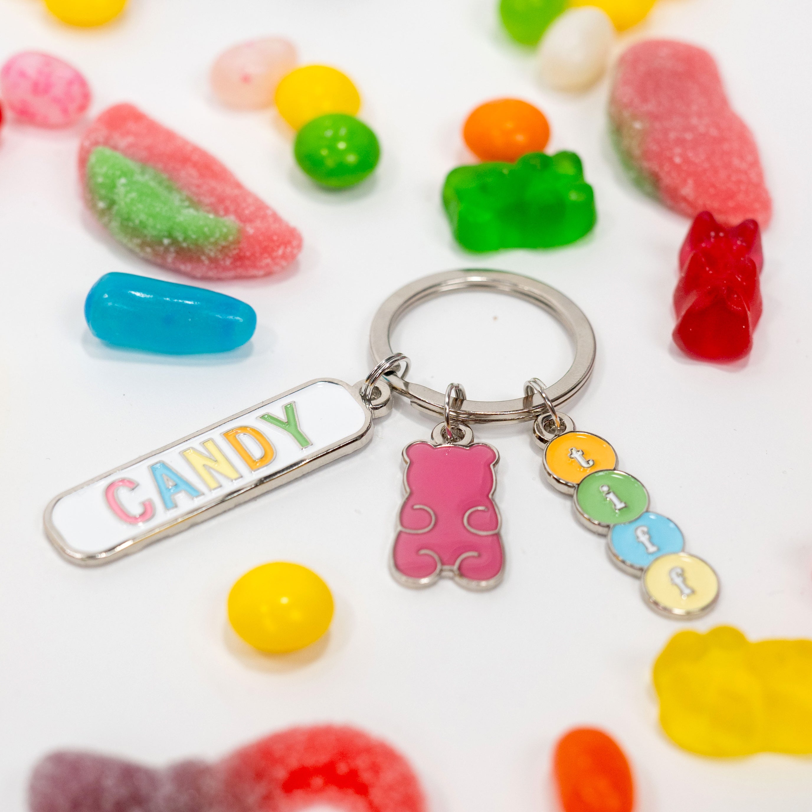 Assorted candy gummies on a white background alongside a silver-tone keychain with three charms: a gummy bear, a “TIFF” tag, and a “Candy” tag.