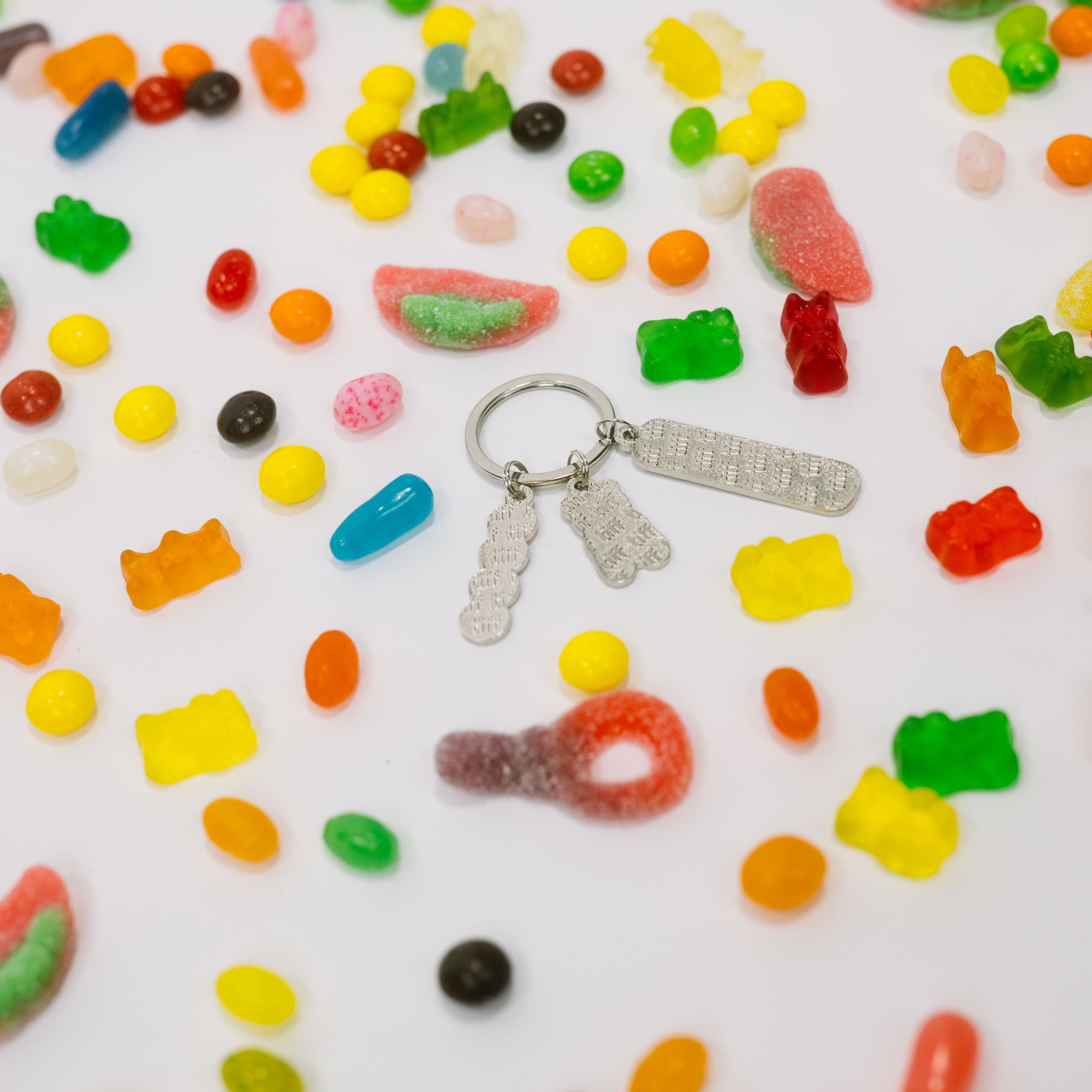 Assorted candy gummies on a white background with the back of silver-tone keychain with "TIFF" embossed charms.
