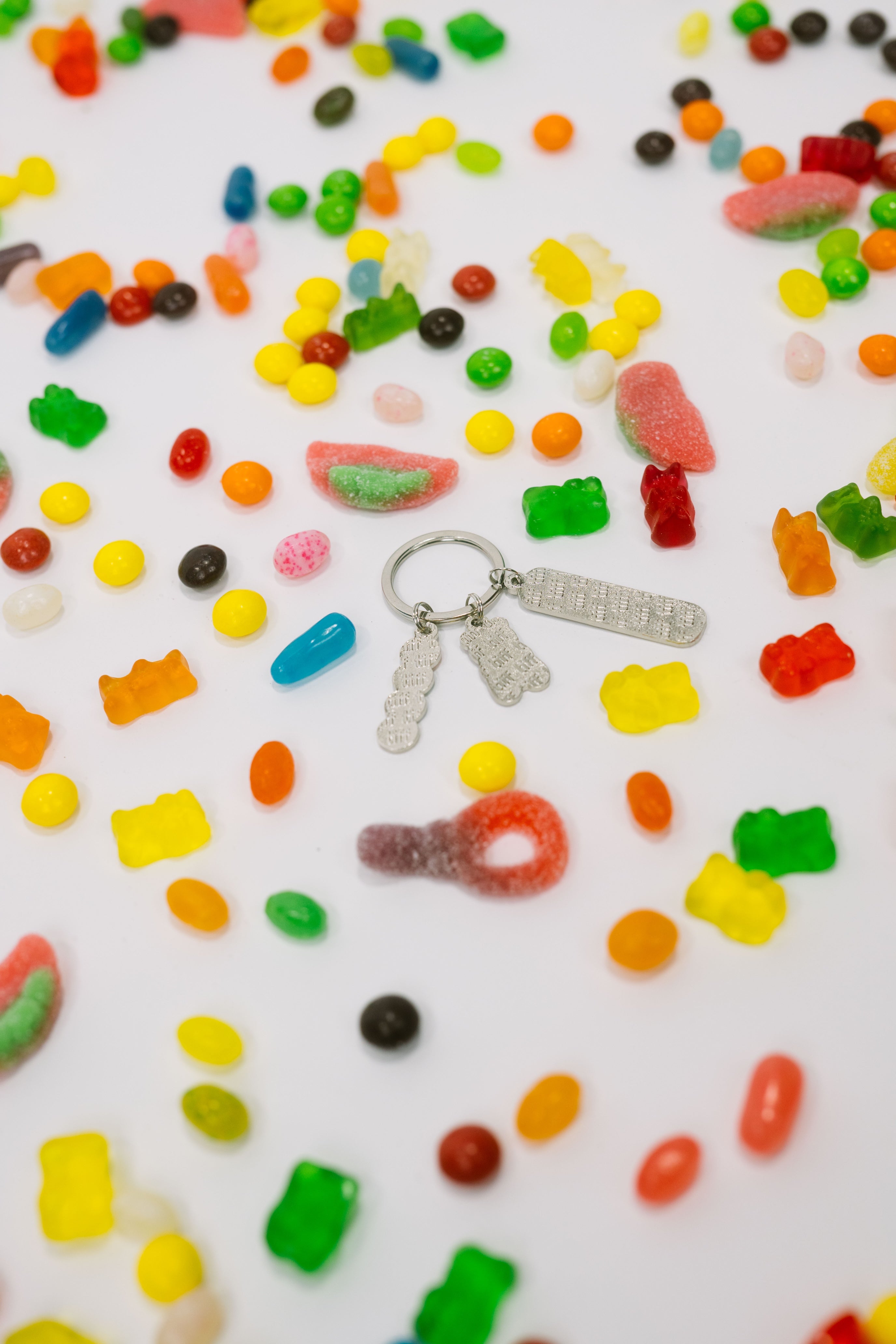 Assorted candy gummies on a white background with the back of silver-tone keychain with "TIFF" embossed charms.