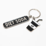 Silver-tone keychain on a white background featuring two charms: a black “Diet Soda” tag and a soda cup with a straw.
