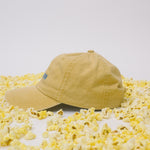 Side profile of yellow baseball cap on a white background surrounded by popcorn.
