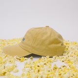 Side profile of yellow baseball cap on a white background surrounded by popcorn.
