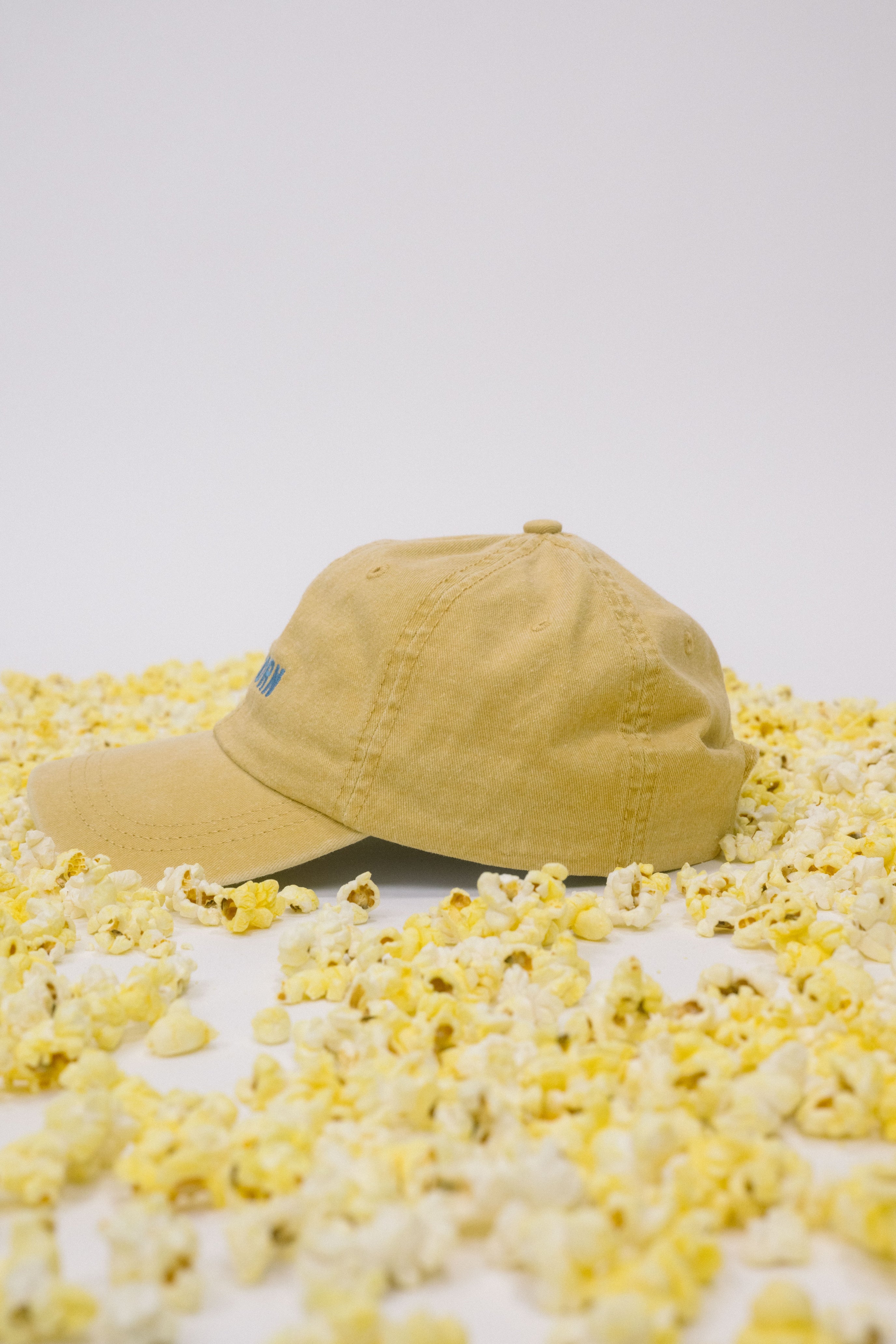 Side profile of yellow baseball cap on a white background surrounded by popcorn.