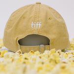 Back view of yellow baseball cap on a white background with popcorn surrounding it, featuring “TIFF” embroidery in white. 