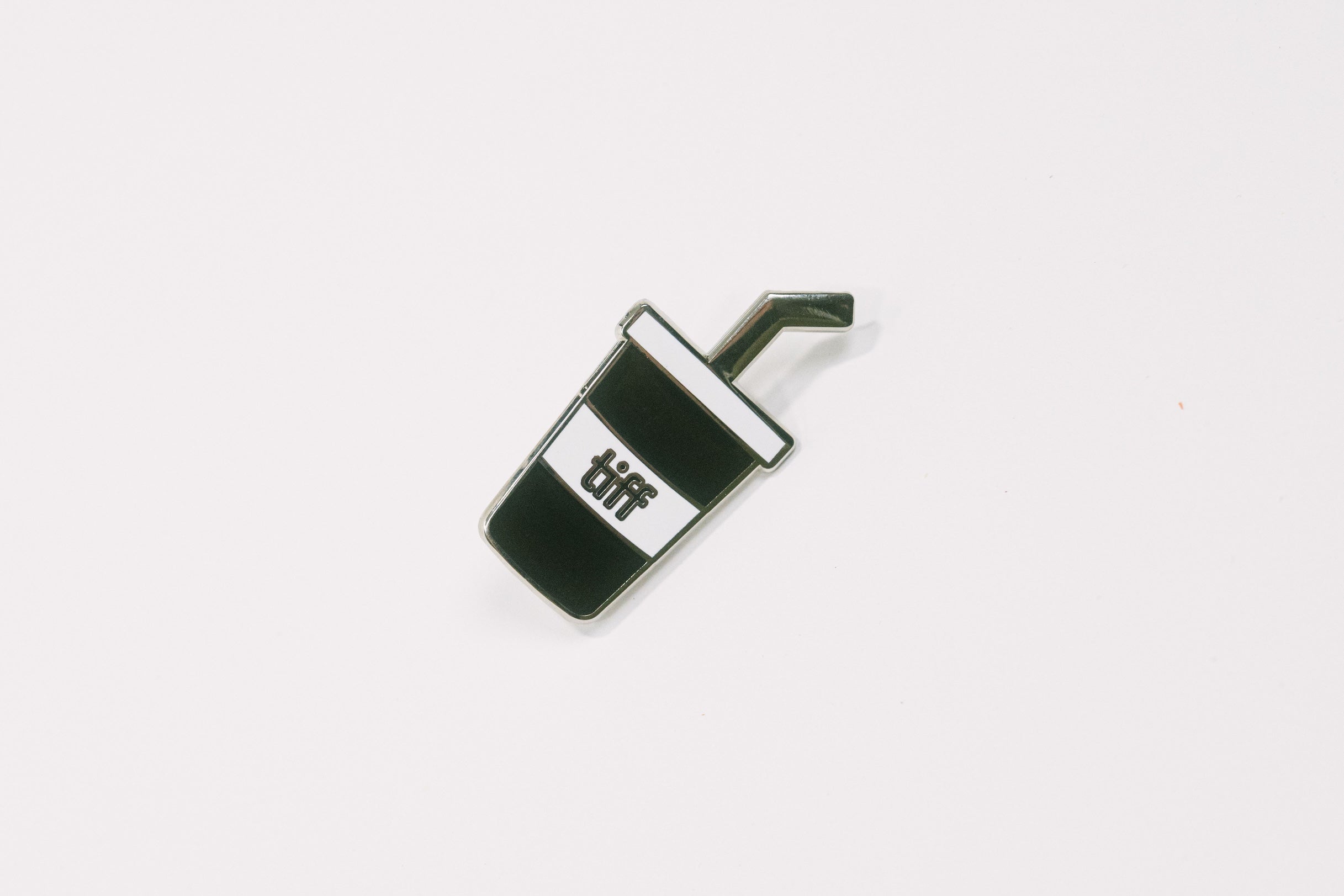 Black and white soda cup shaped enamel pin with the TIFF logo at center on a white background.