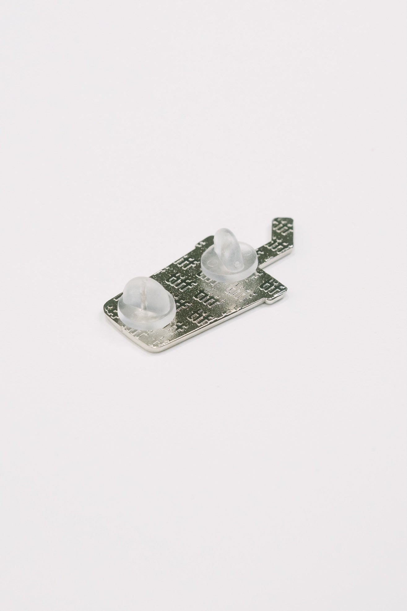 Back view of a soda cup shaped enamel pin in silver on white background, featuring an embossed TIFF monogram with silicone backings.