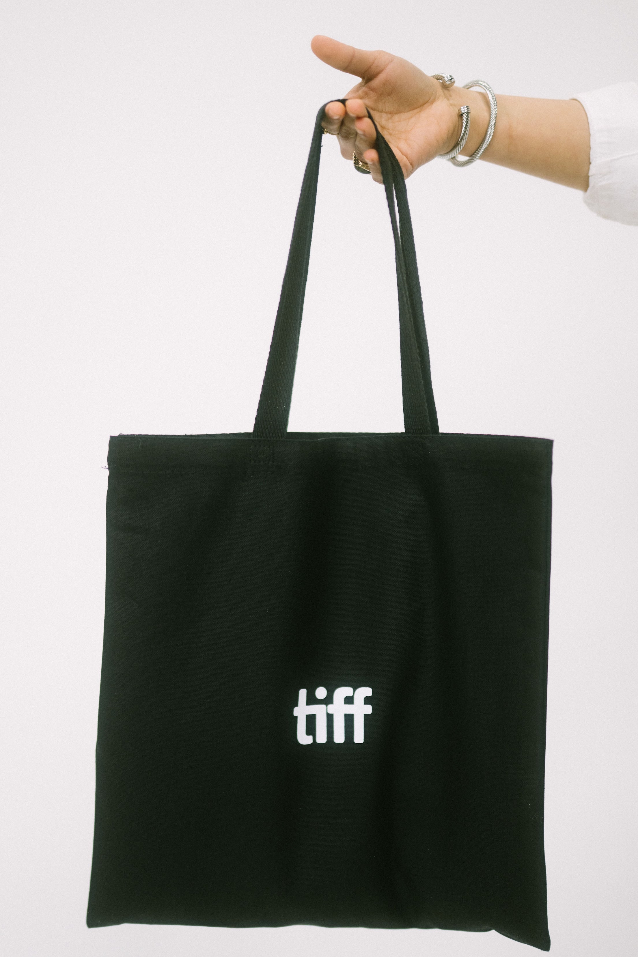 Black tote bag with 'tiff' logo held by a hand on a white background