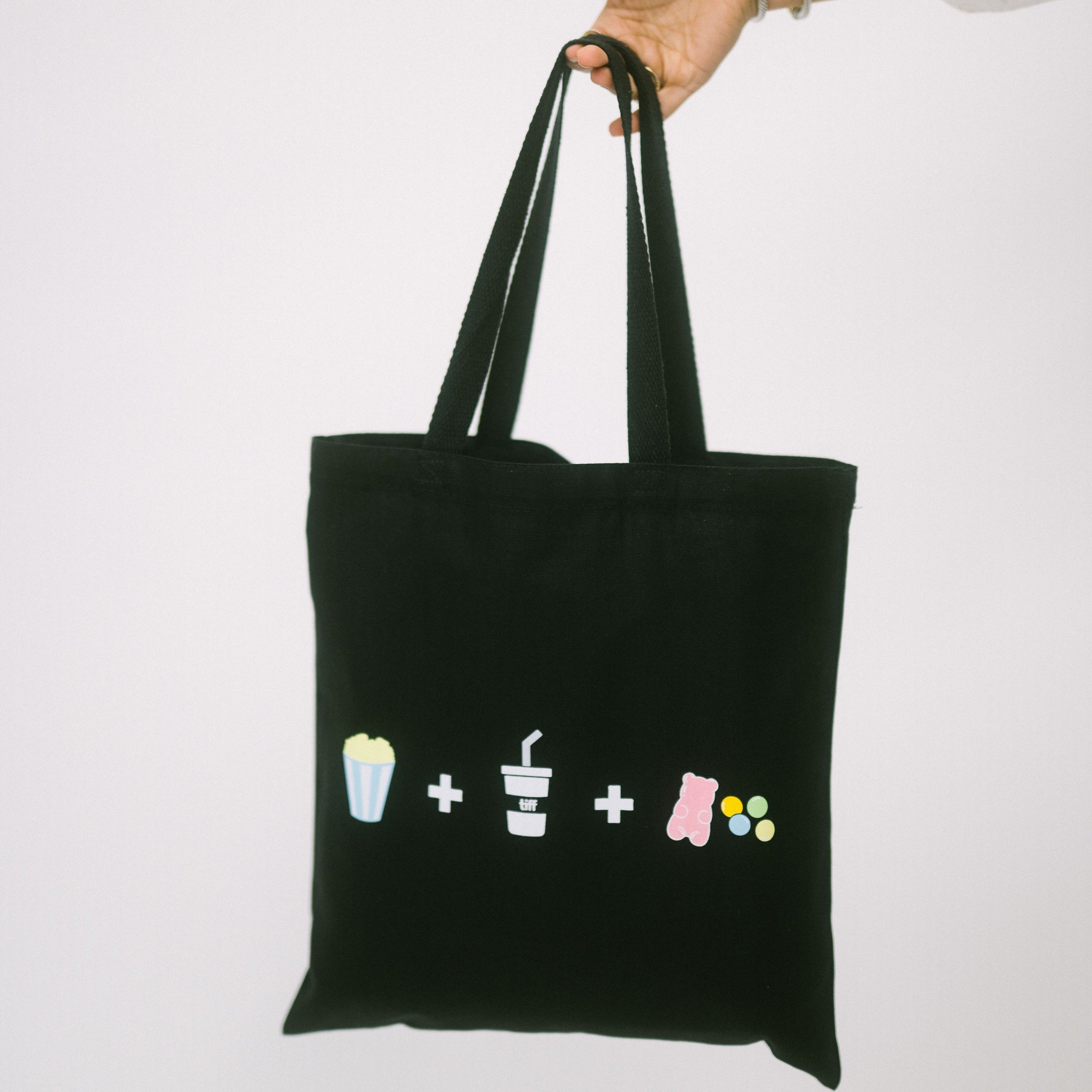 Black tote bag with colorful symbols held by a person on a white background