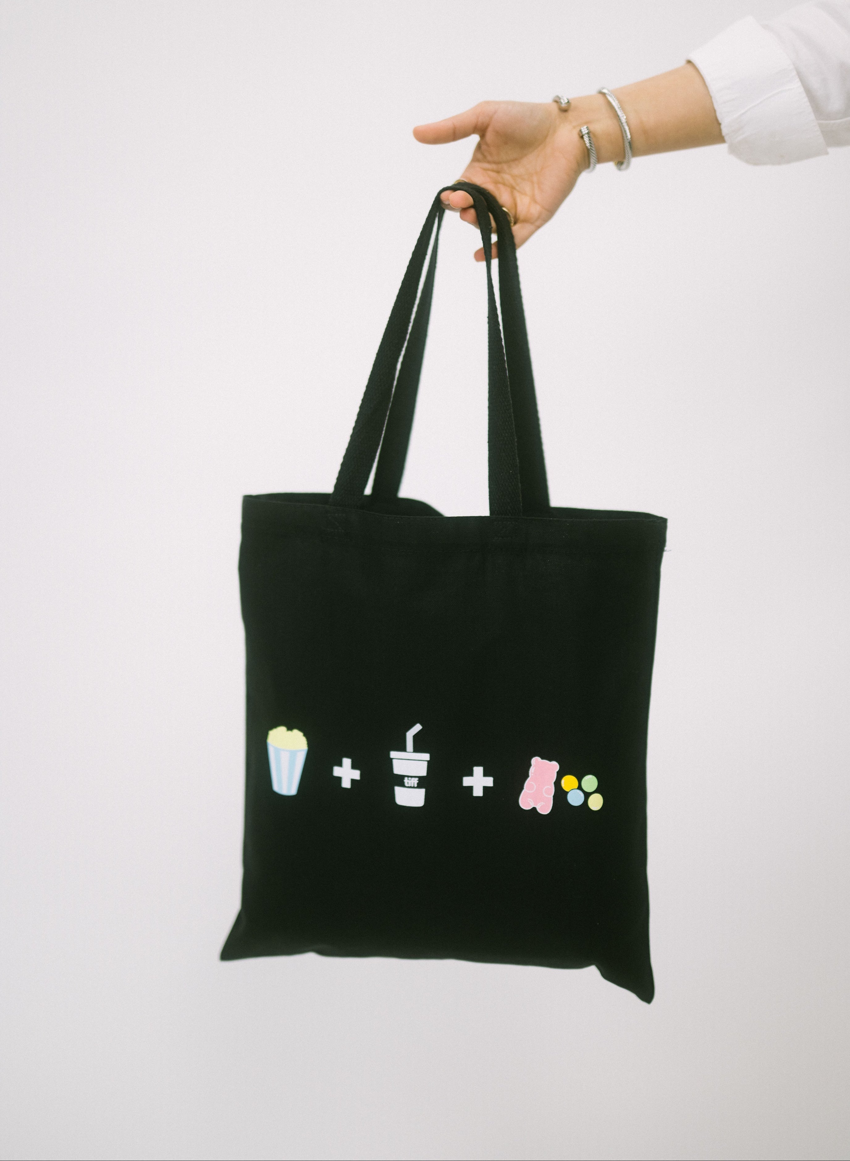 Black tote bag with colorful symbols held by a person on a white background