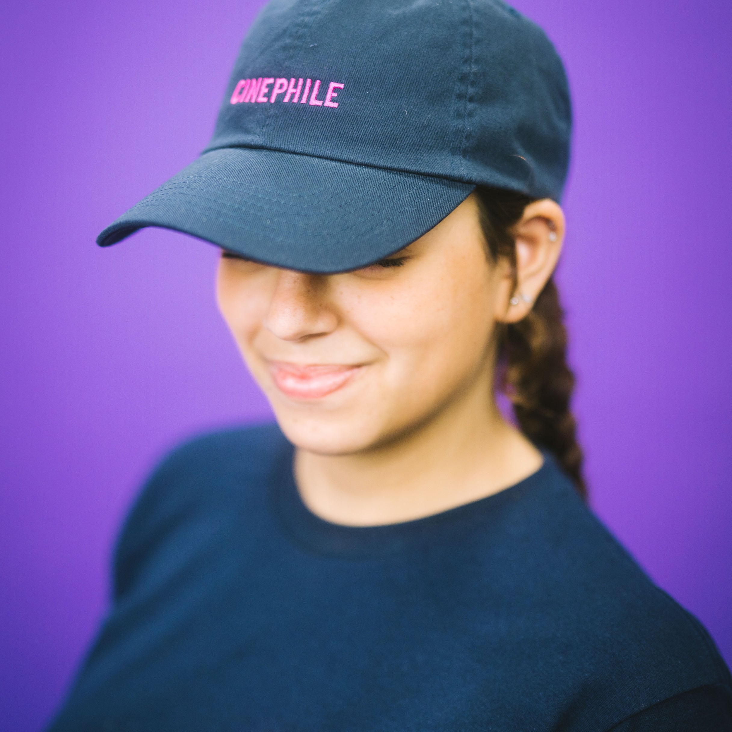 Person wearing a blue cap and black t-shirt with text against a purple background