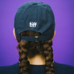 Person wearing a blue cap with 'tiff' on a purple background