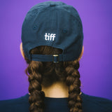 Person wearing a blue cap with 'tiff' on a purple background