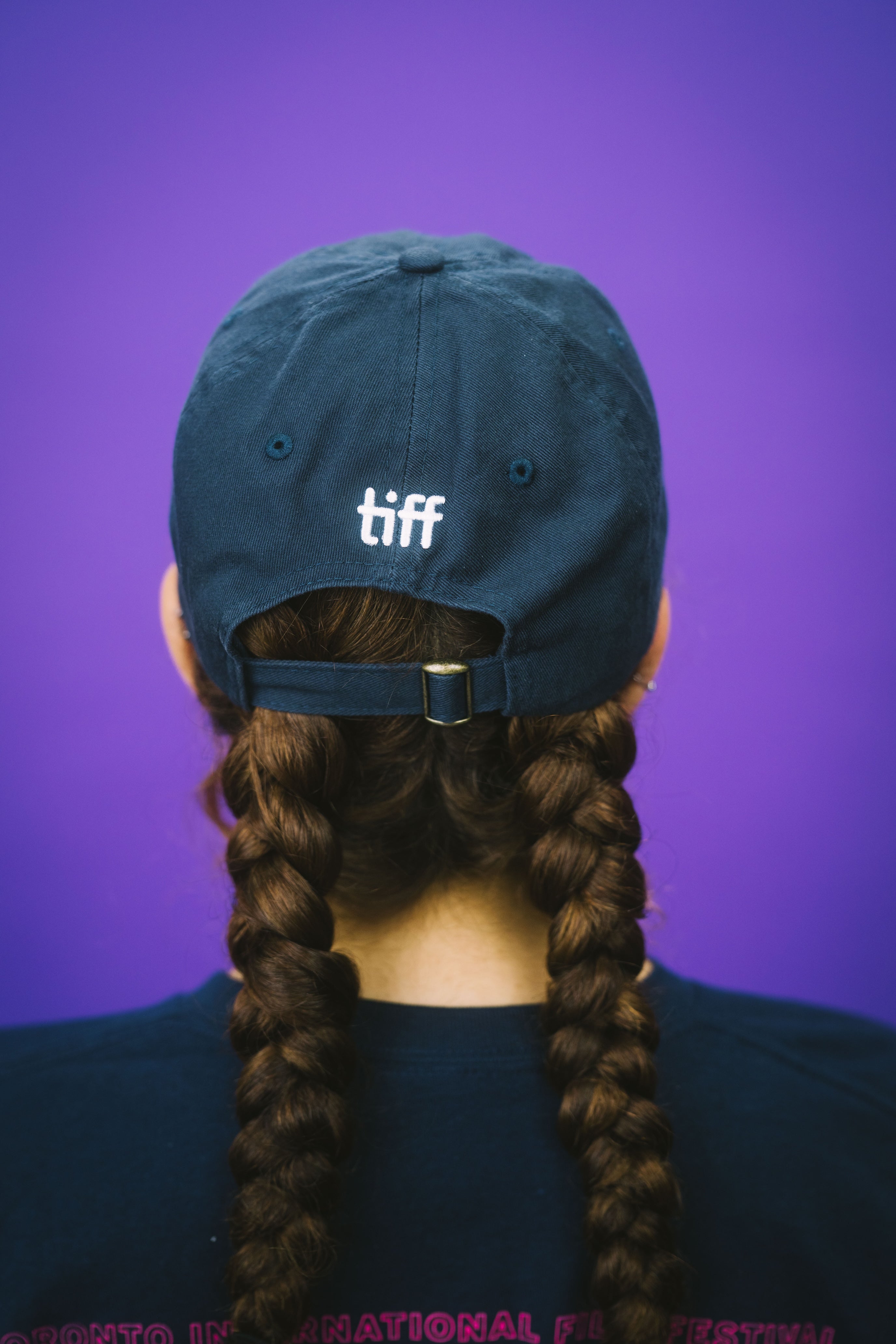 Person wearing a blue cap with 'tiff' on a purple background