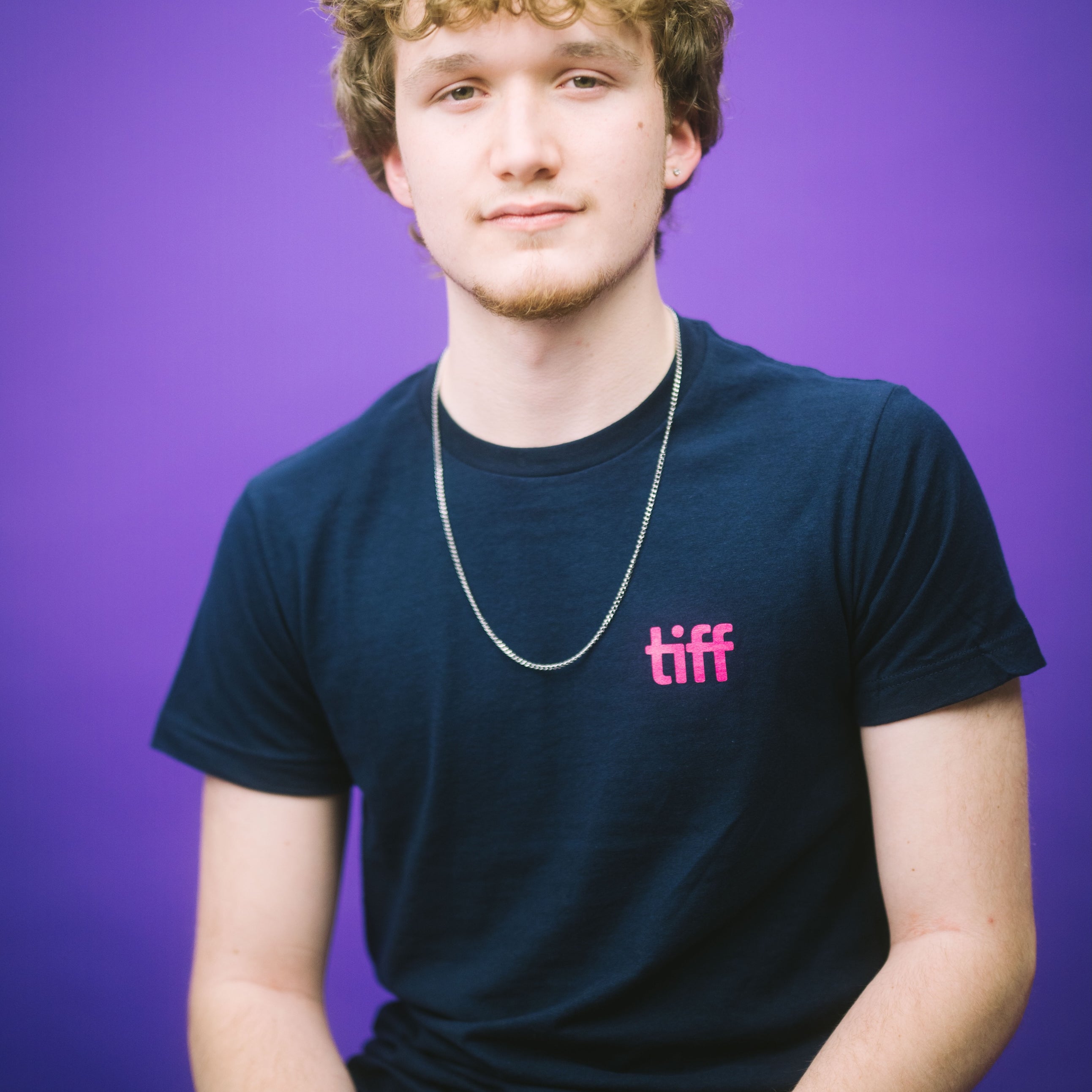 Person wearing a black t-shirt with 'tiff' logo against a purple background