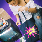 Person holding a tote bag with 'I love movies' design on a purple floor with a vintage television and CDs.