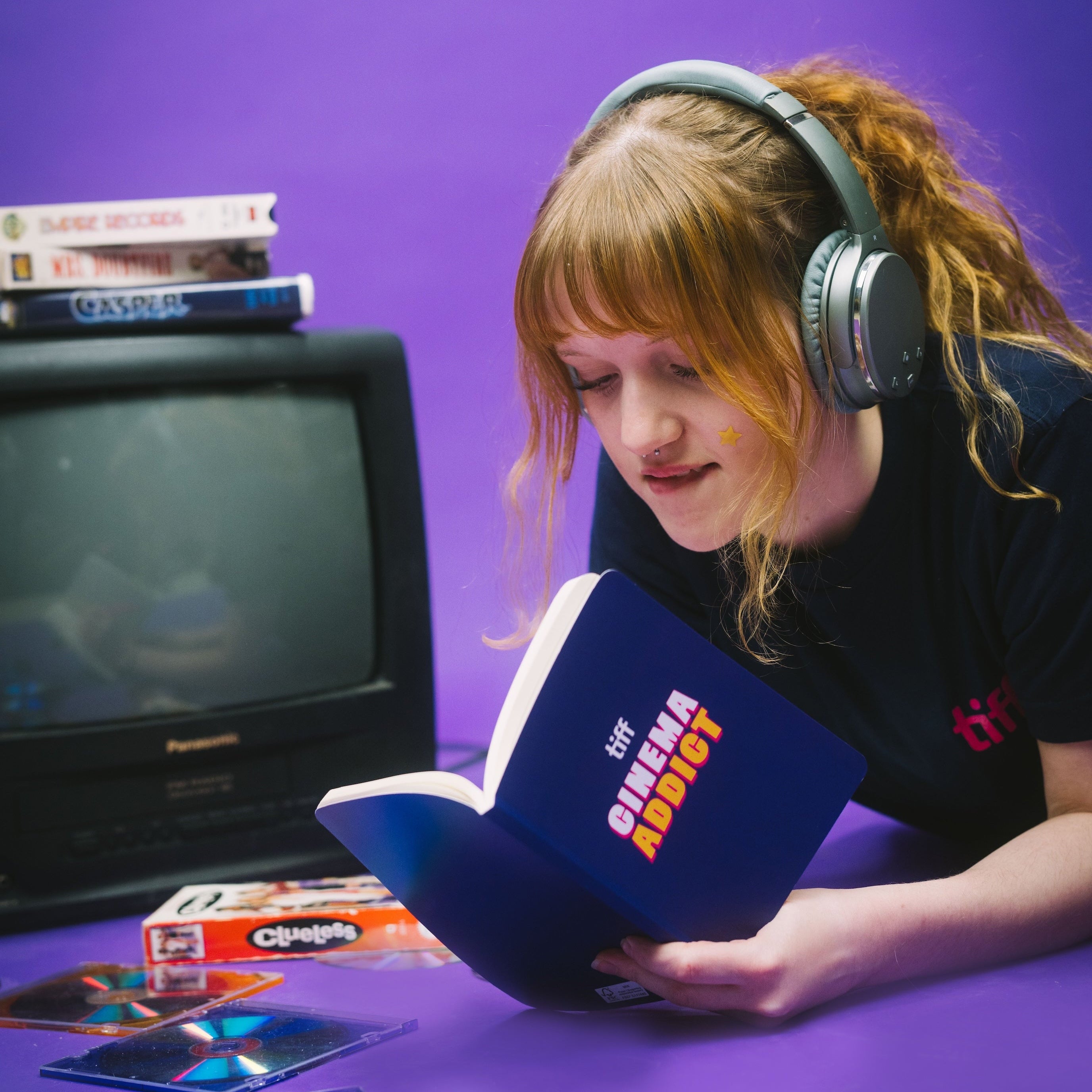 Person wearing headphones and holding a book with a purple background