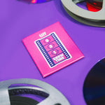 Pink 'tiff' Next Wave magnet with film reels on a purple background