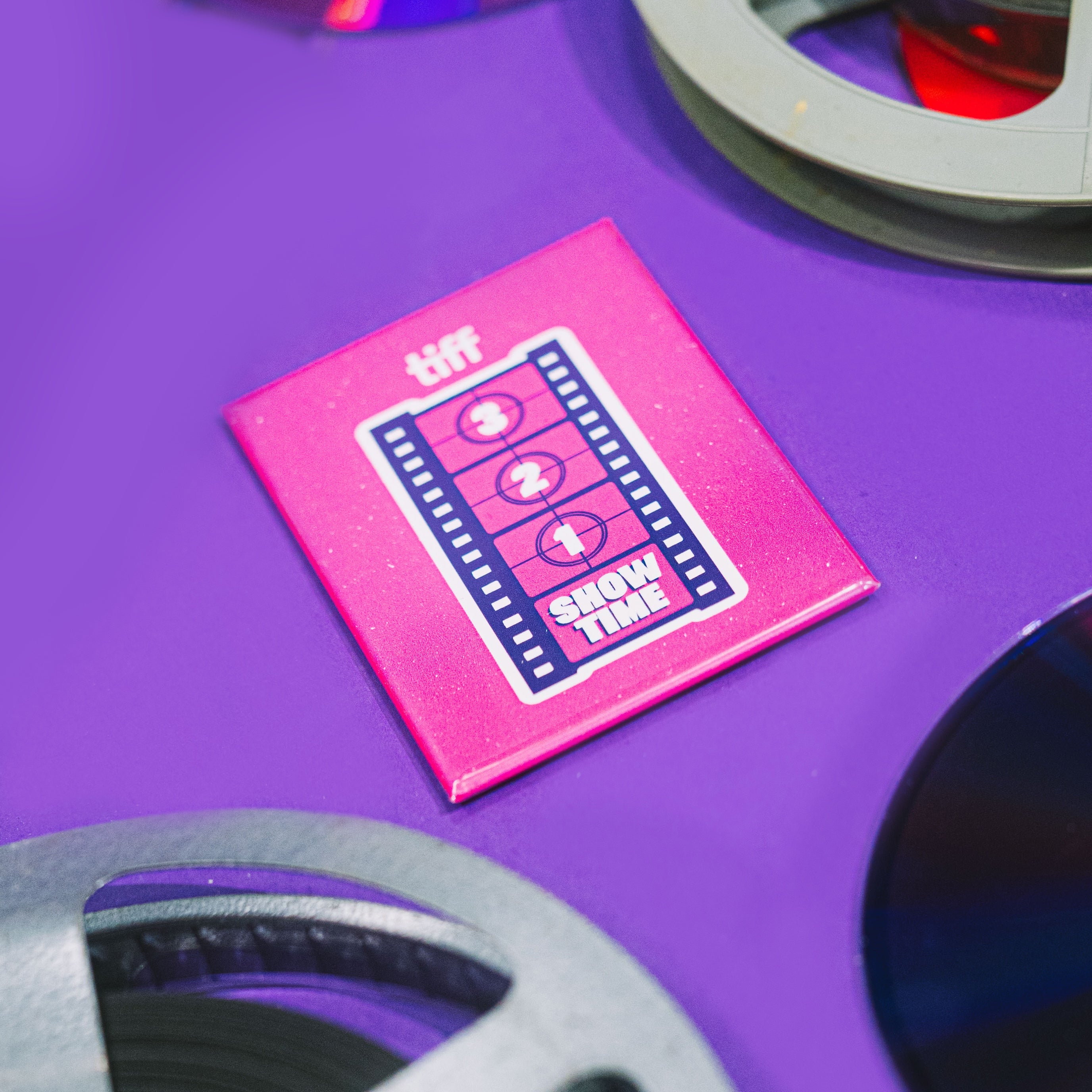 Pink 'tiff' Next Wave magnet with film reels on a purple background
