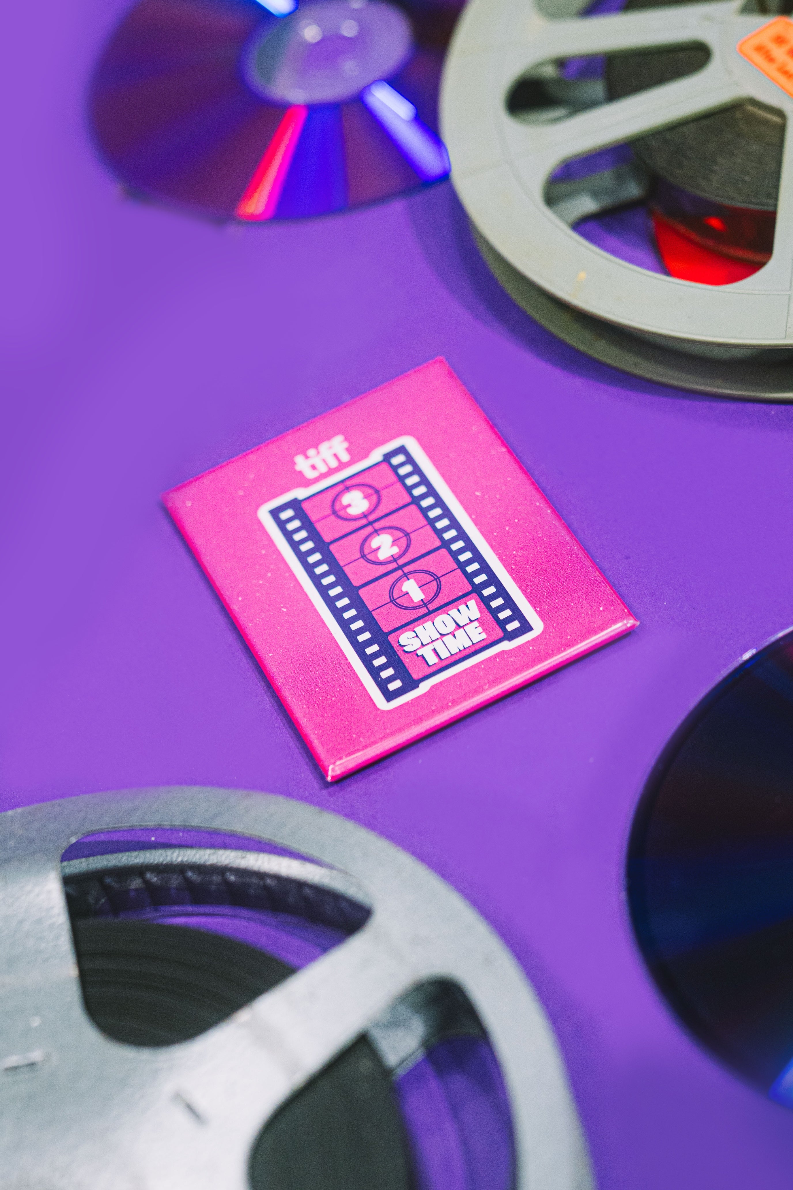 Pink 'tiff' Next Wave magnet with film reels on a purple background