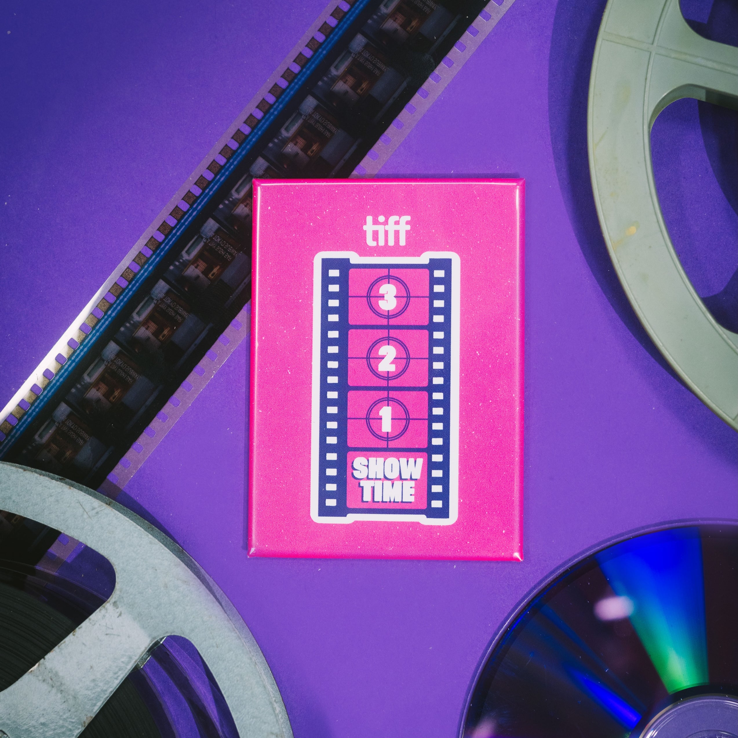 Pink 'tiff' Next Wave magnet with film reels on a purple background