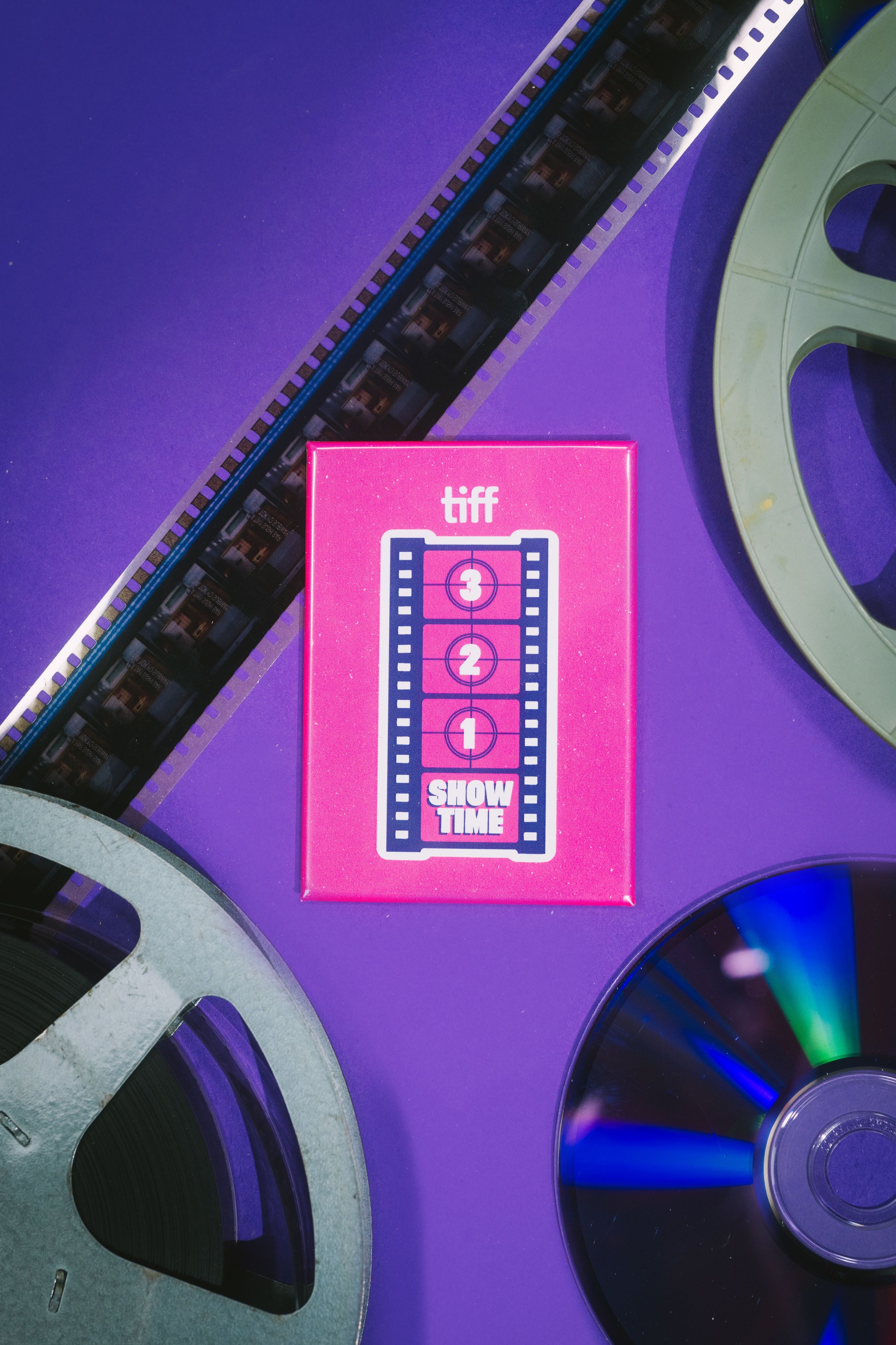 Pink 'tiff' Next Wave magnet with film reels on a purple background