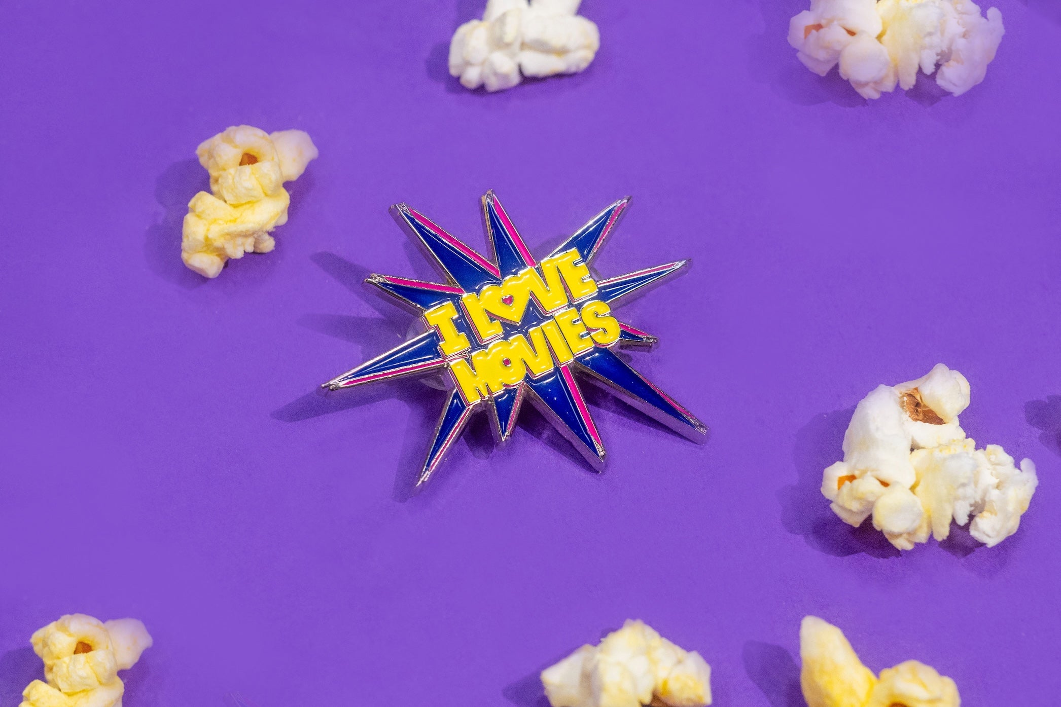 Pin with 'I Love Movies' text surrounded by popcorn on a purple background