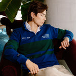 A man wearing a blue and green striped quarter-zip pullover sweater with 'EST. 1975' and 'TORONTO INTERNATIONAL FILM FESTIVAL' printed on the chest, sitting in a red armchair.