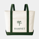 A cream-colored canvas tote bag featuring dark green vertical straps and a matching base, with a central pocket displaying a green botanical illustration above the word "HAMNET" in bold, green serif letters.