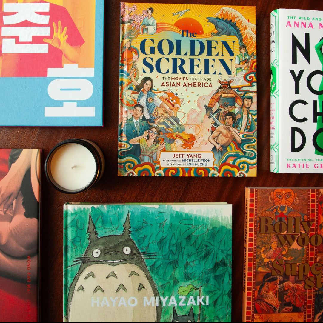 Display of Asian Heritage books on brown wood counter with cream coloured candle .