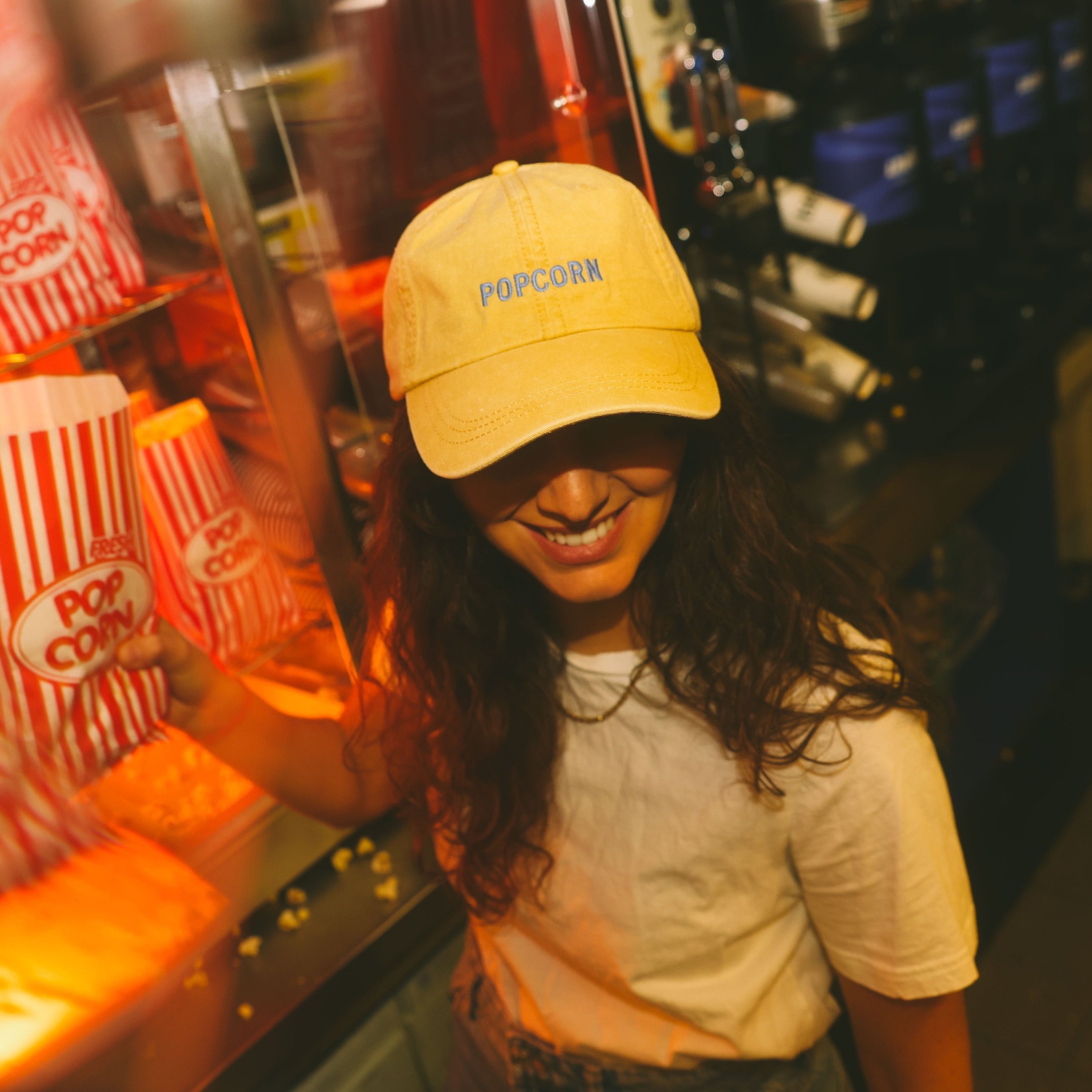 Person wearing a yellow 'Popcorn' cap in front of a popcorn machine.