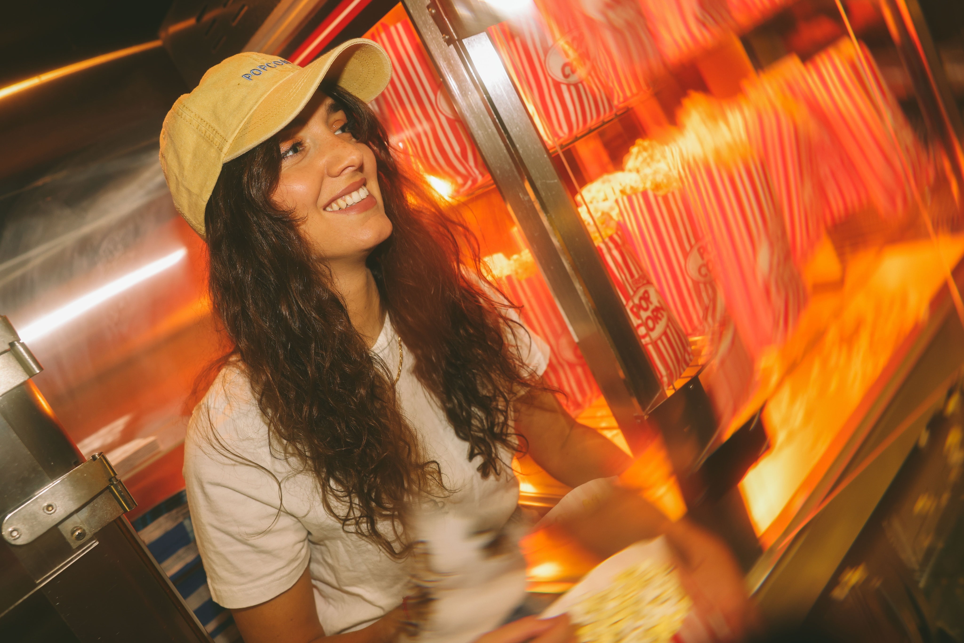 Woman in a yellow cap smiling in front of a popcorn machine