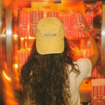 Person wearing a yellow 'POP CORN' cap in front of a popcorn machine.
