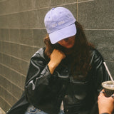 Two people standing against a gray wall, one holding a drink.